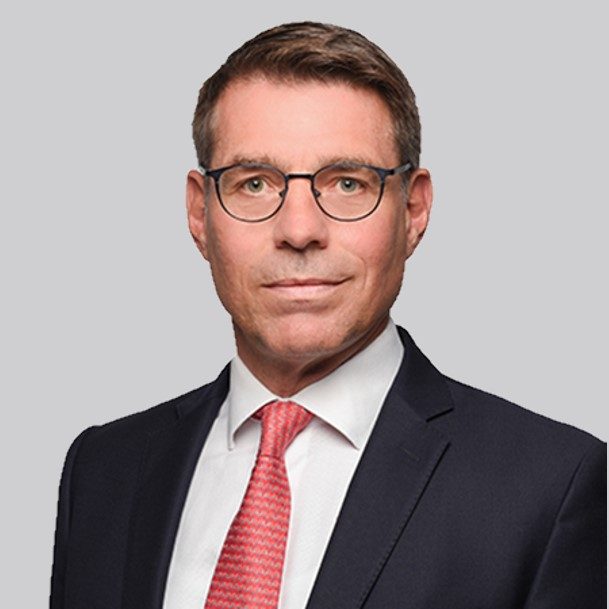 Die Person trägt einen dunklen Anzug mit weißem Hemd und roter Krawatte.